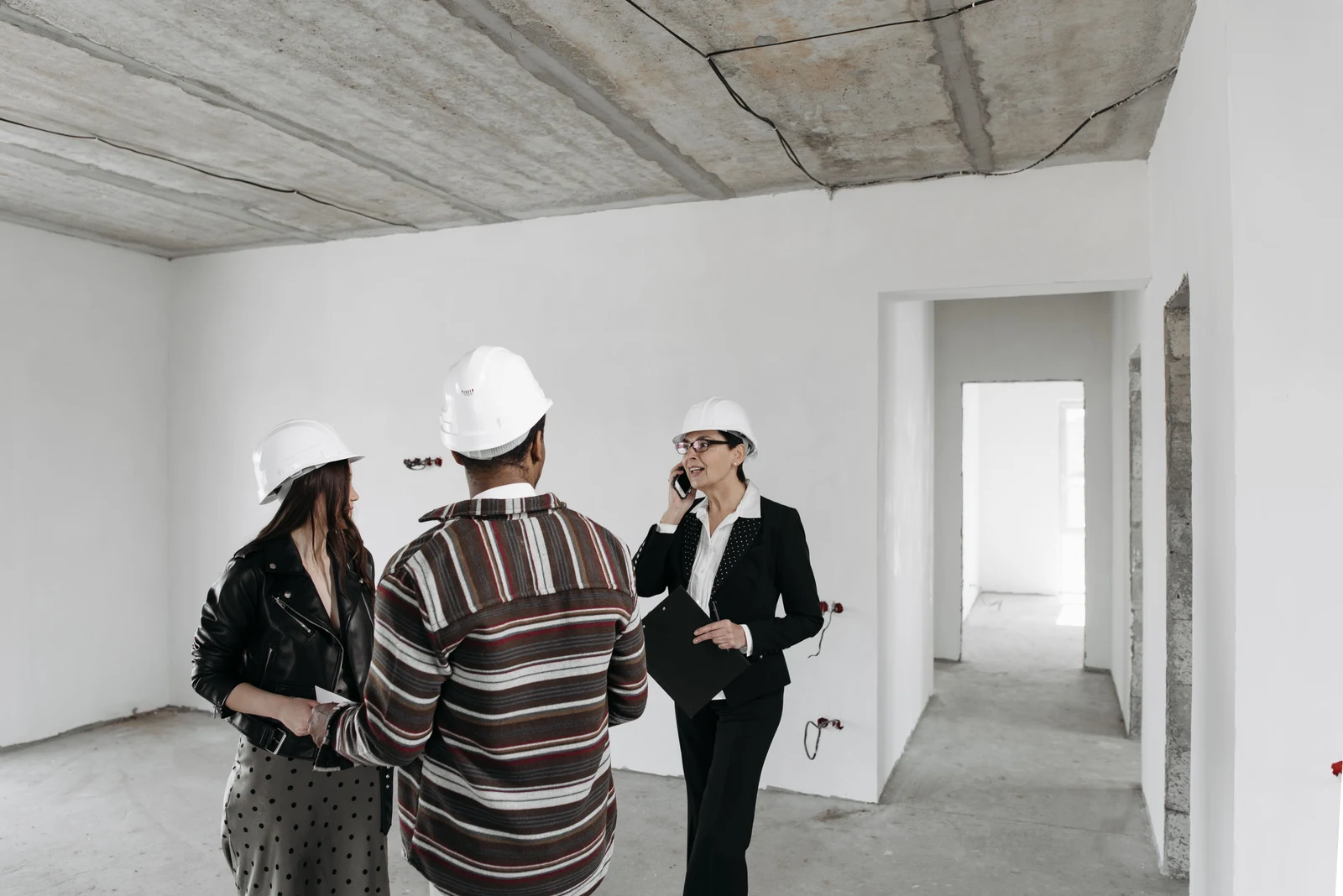 Builder and homeowners in hard hats reviewing a new construction walk-through