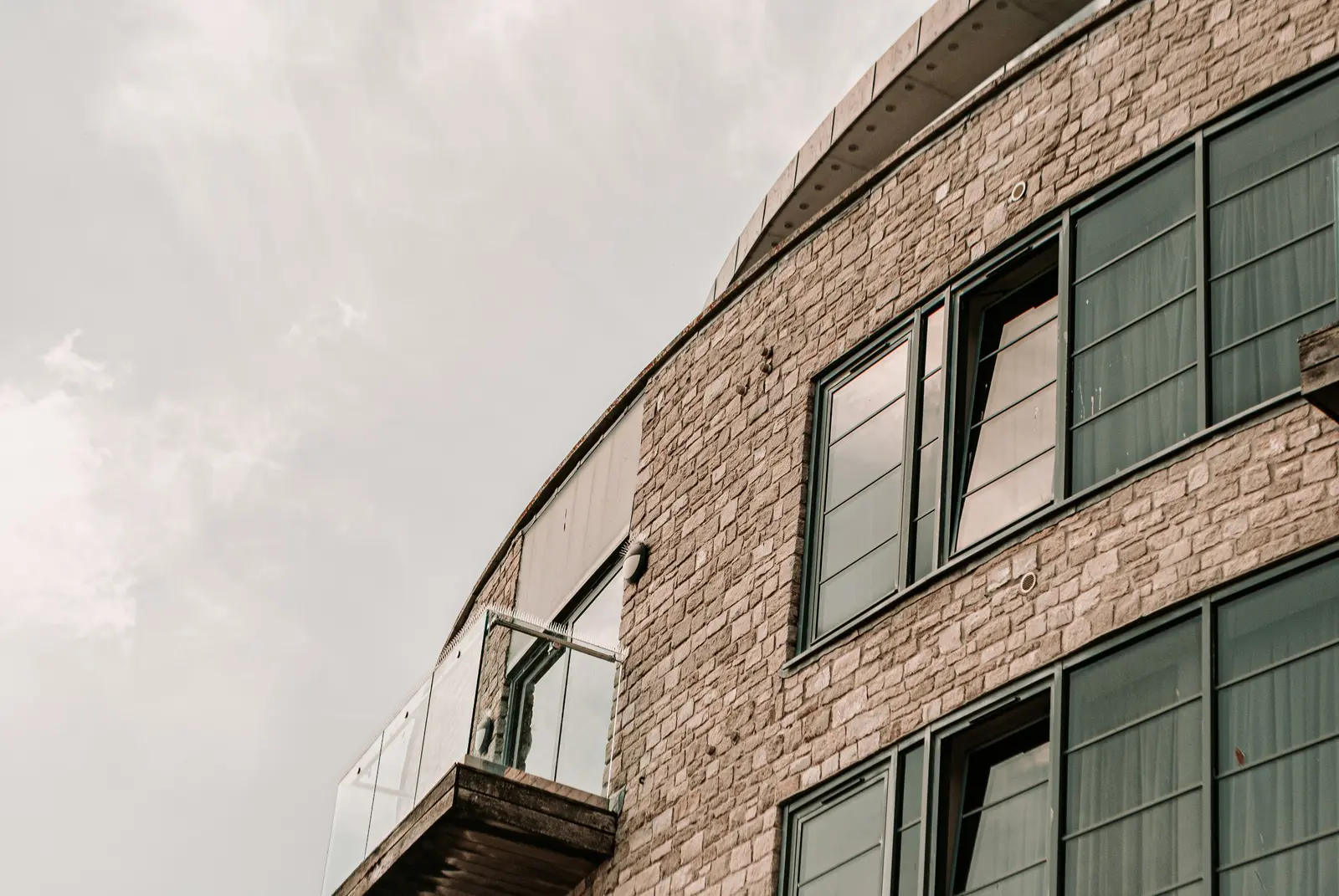 Modern curved stone masonry veneer facade with glass balconies on a commercial building